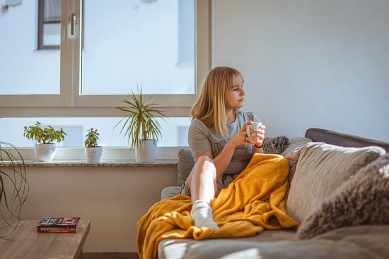 Frau sitzt entspannt auf dem Sofa am Abend mit einer Tasse Tee – bewusst entspannen statt abends snacken.