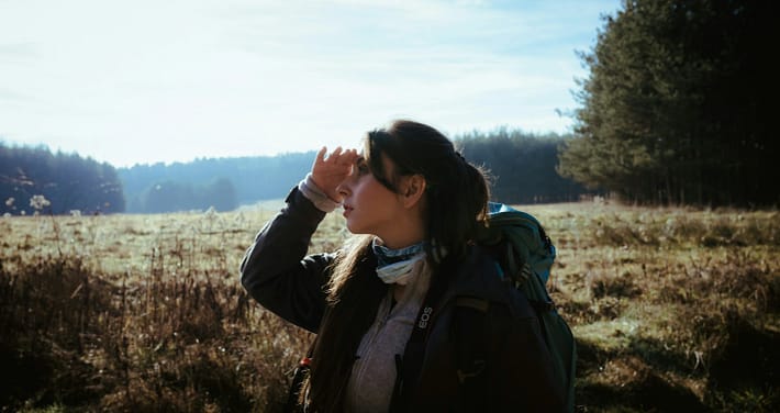Frau geht am Feldrand in der Abendsonne und blickt nach vorn – achtsam unterwegs