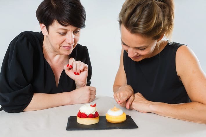 Zwei Frauen betrachten konzentriert kleine Törtchen – Symbol für bewussten Genuss ohne Diät-Zwang