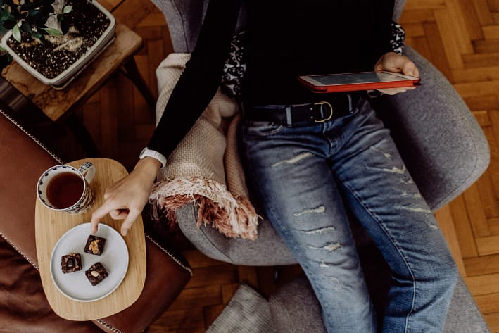 Frau sitzt abends auf der Couch mit Tee und kleinen Schokoladenstücken – Symbol für Heißhunger am Abend