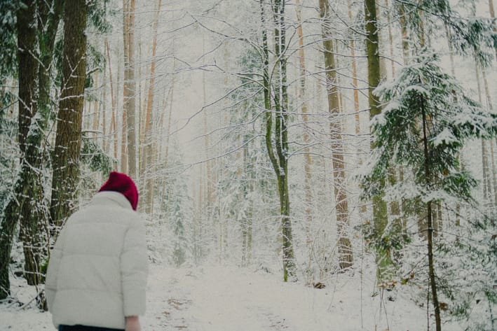 Person geht ruhig durch einen verschneiten Wald – ein stiller Moment zum Durchatmen