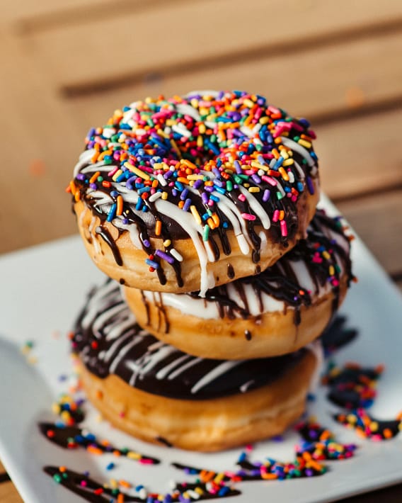 Drei übereinander gestapelte Donuts mit Schokoglasur und bunten Streuseln – symbolisch für emotionales Essen und Heißhungerattacken